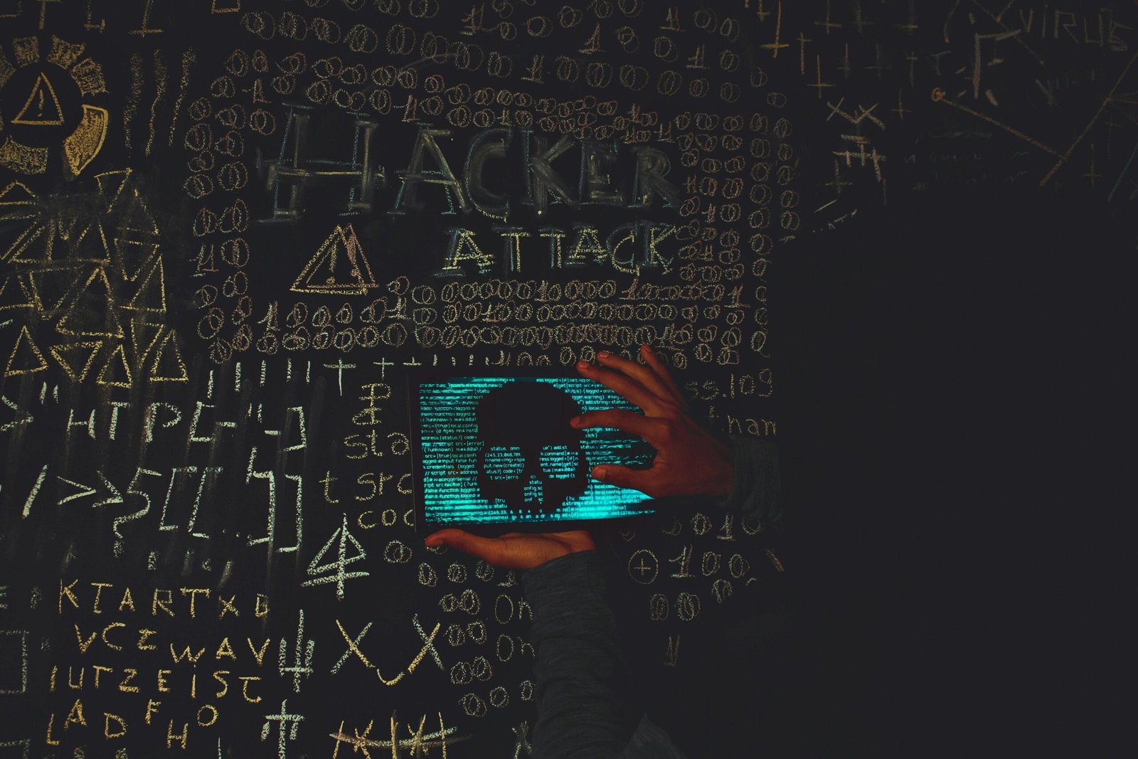 A hacker in a black hoodie using a tablet displaying a skull, surrounded by chalk symbols and 'Hacker Attack' text.