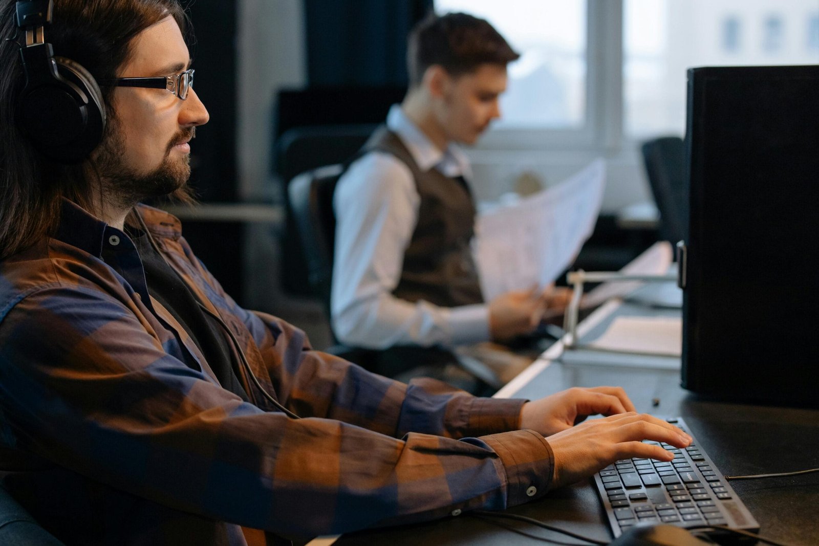 Two office workers focused on tasks at their desks in a modern workspace.