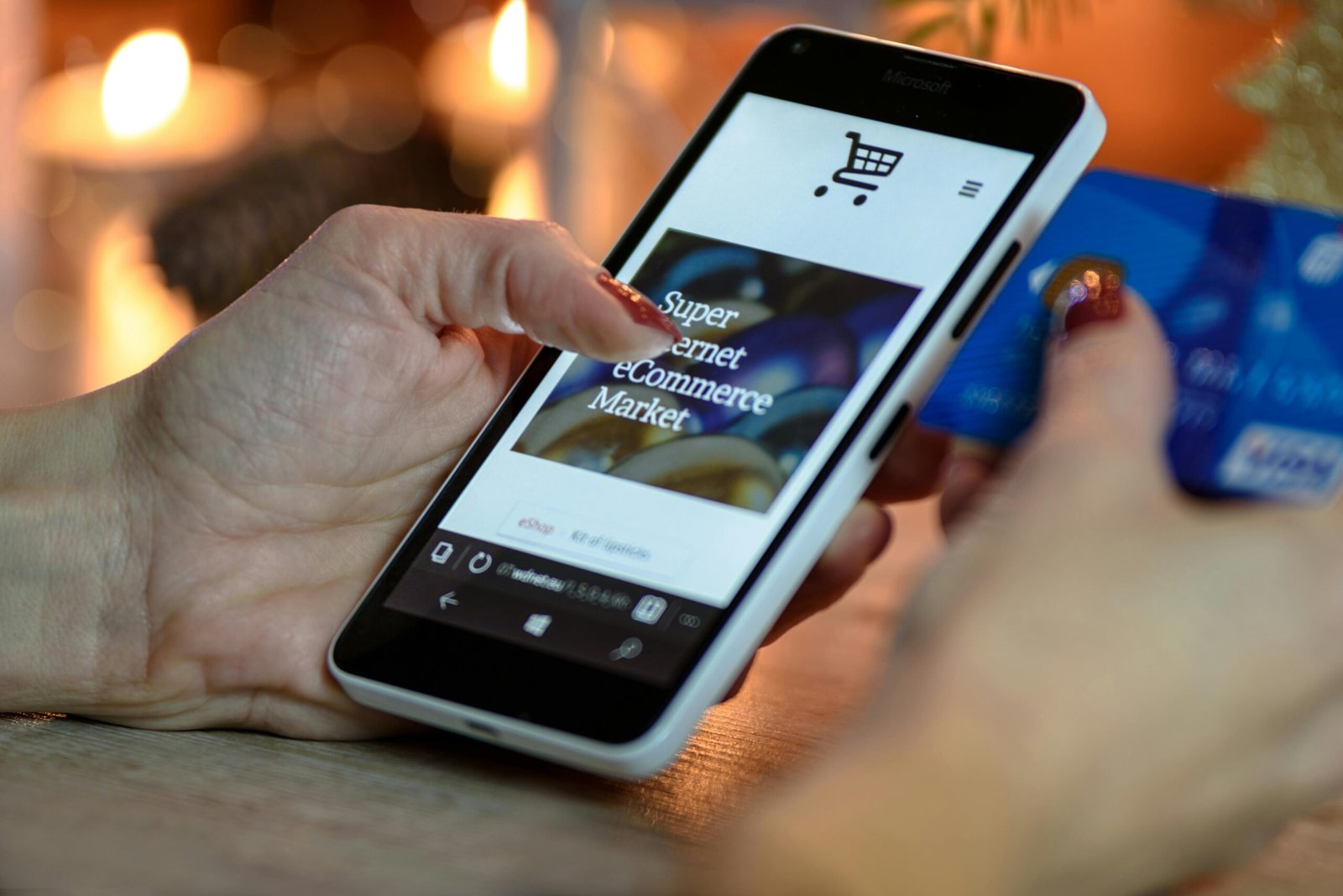 Woman using smartphone for online shopping with credit card in hand, festive background lighting.