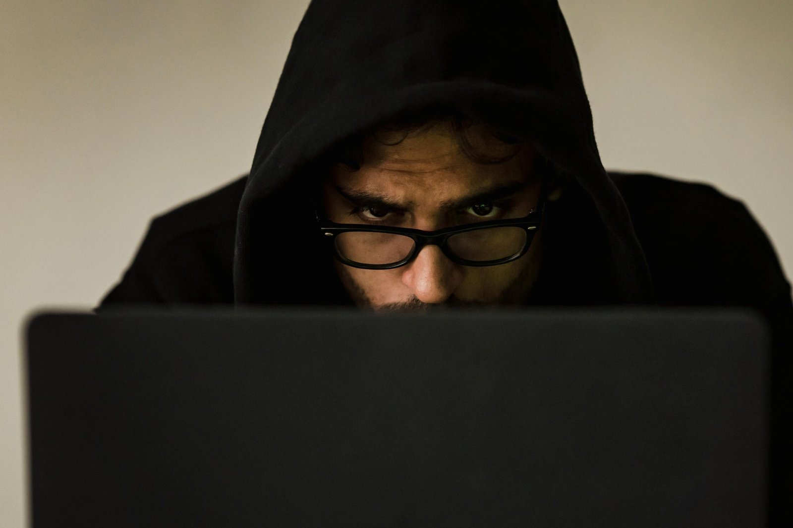 Serious young male programmer wearing black hoodie browsing netbook and hacking software in studio