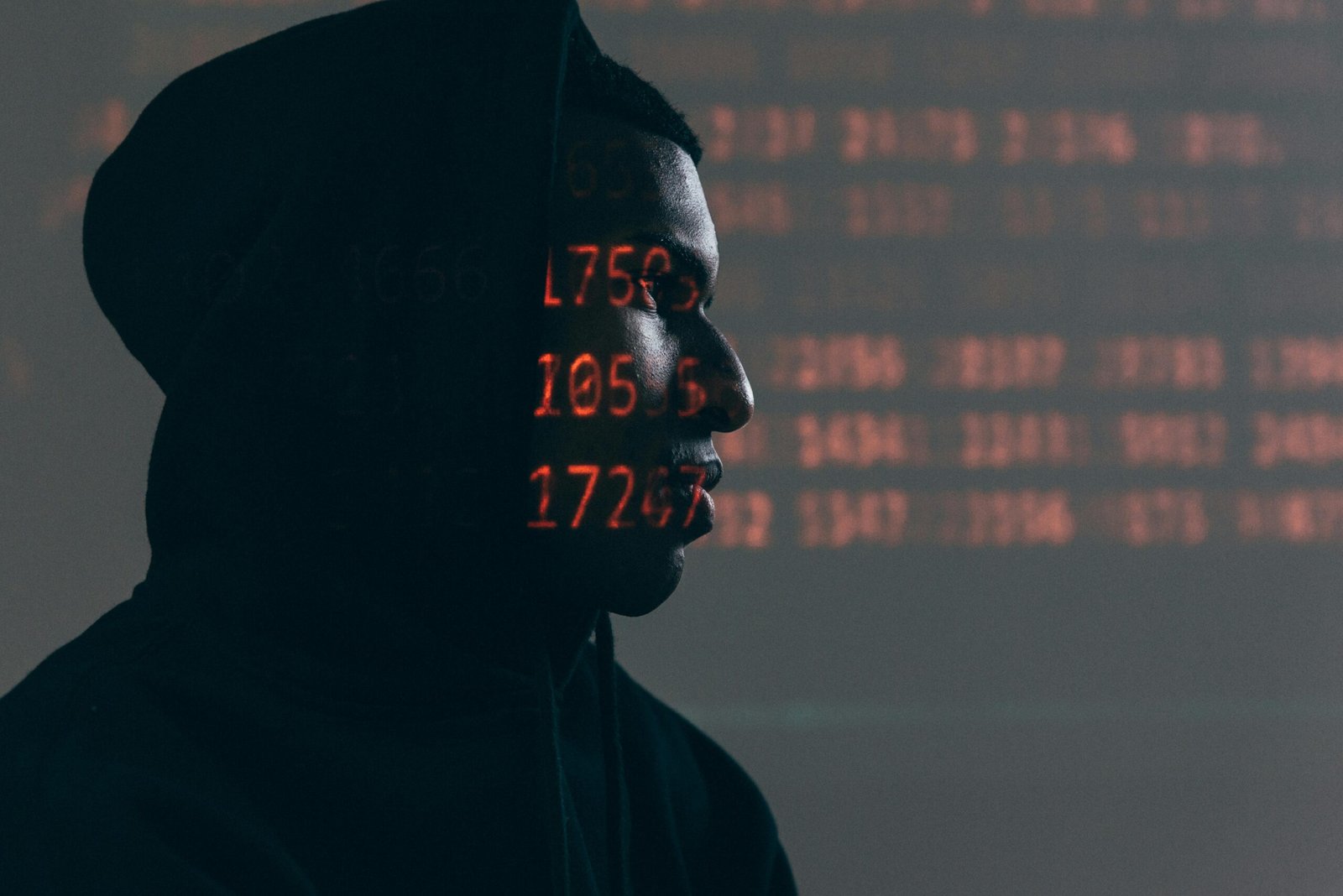 Side profile of a man in a hoodie, surrounded by red code, depicting cybersecurity theme.